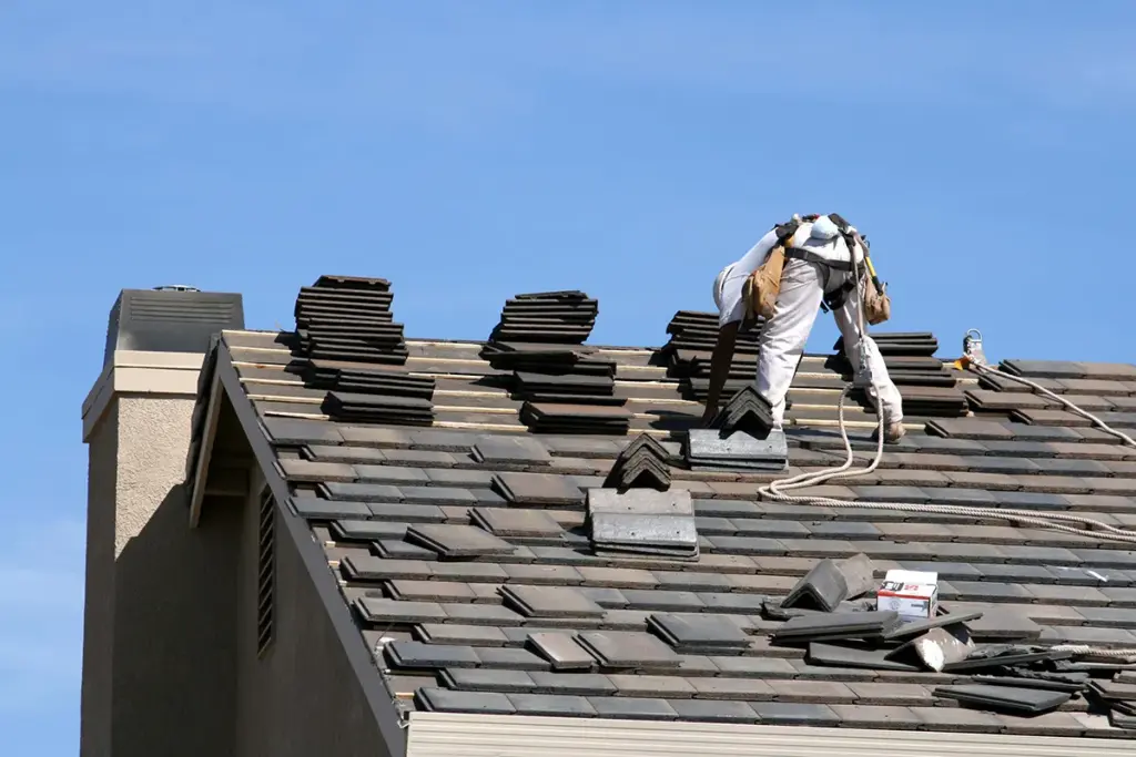 Roofer tearing off old shingles on a steep roof