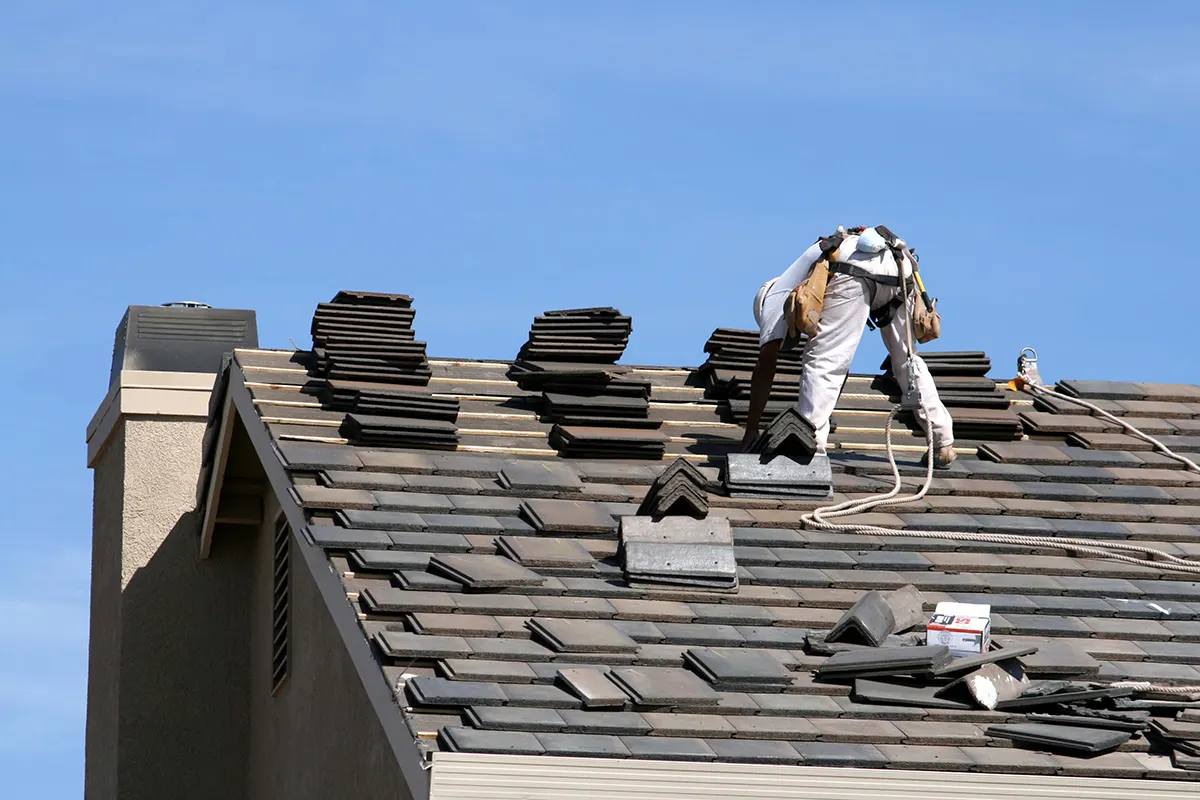 Roofer tearing off old shingles on a steep roof