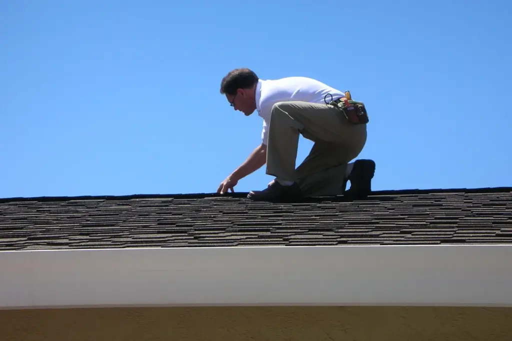 Roofer kneeling on a shingle roof above the fascia