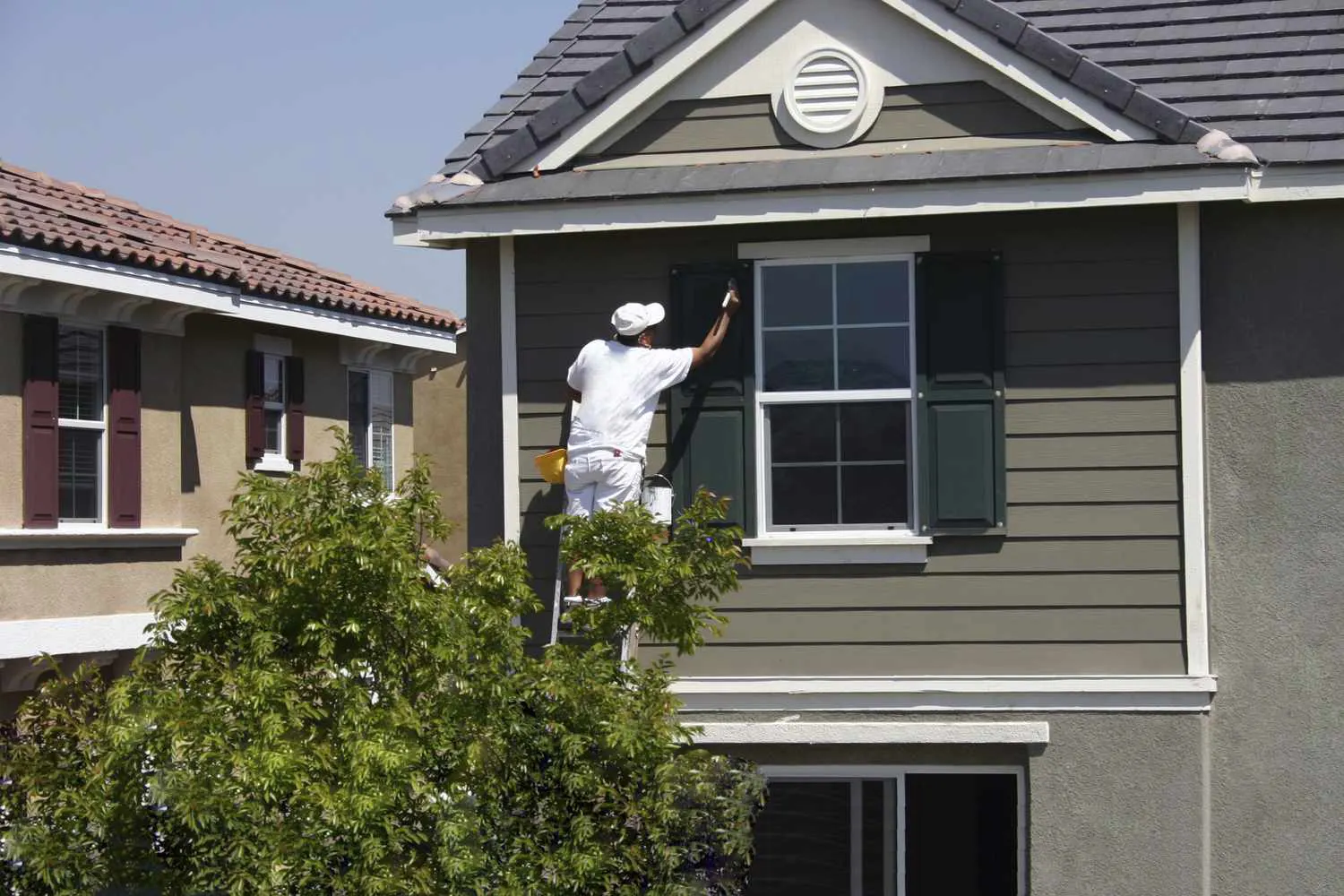 Worker on a ladder installing siding on a two-story house