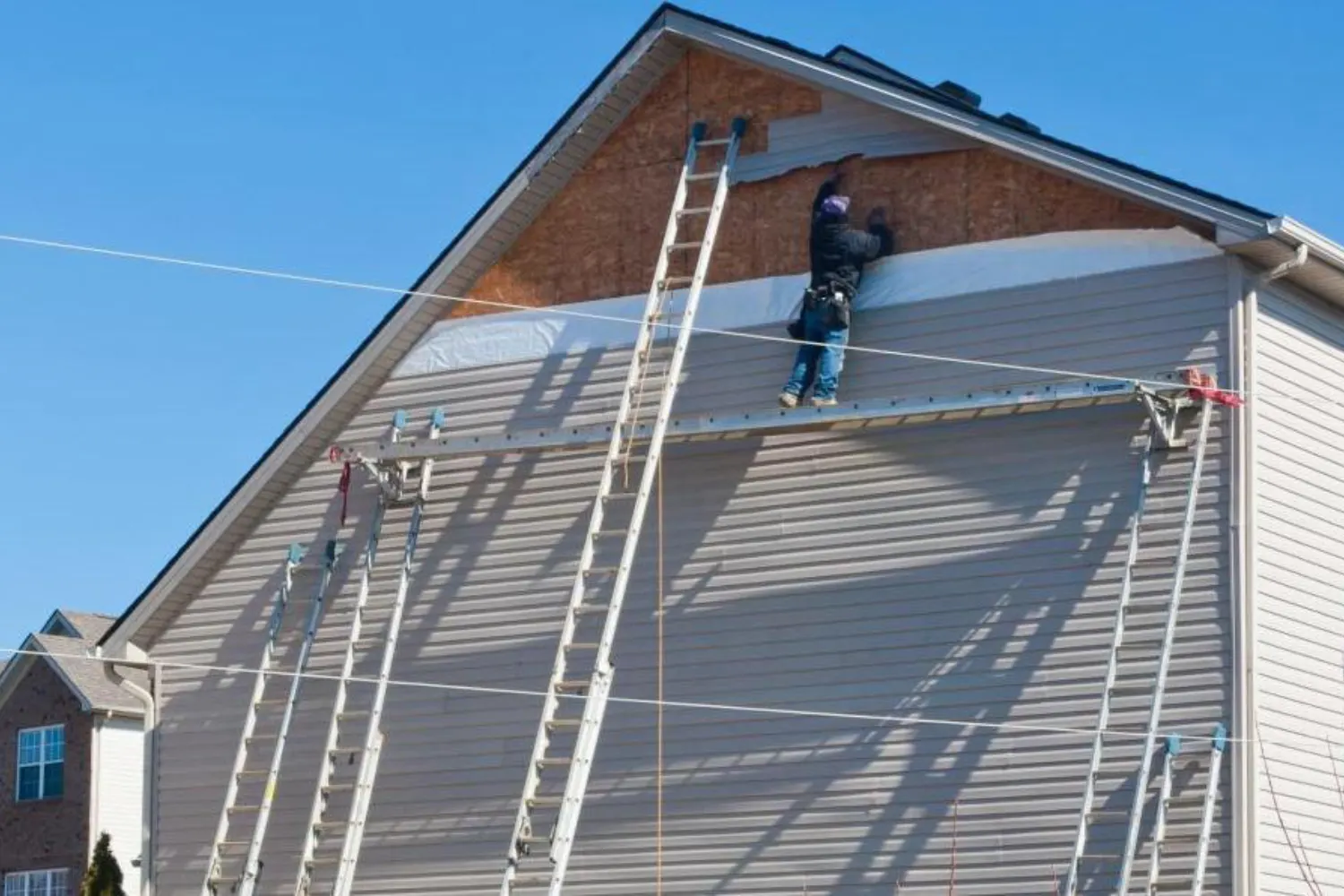 Crew on ladders installing siding on a two-story gable wall