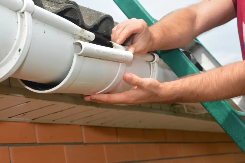 Installer fitting a white downspout elbow to a gutter