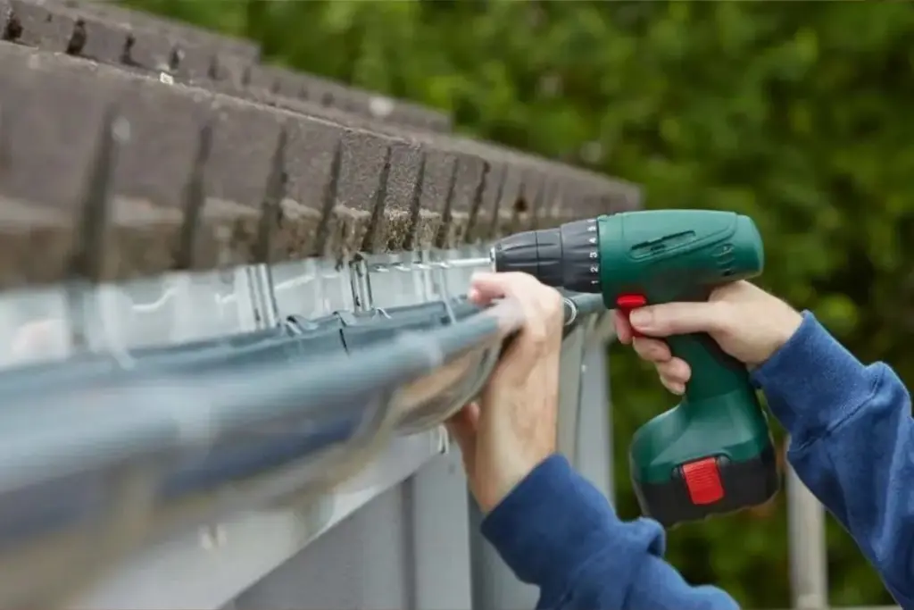 Installer using a cordless drill to fasten a gutter to the roof edge