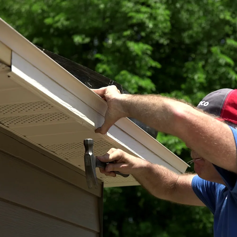 Worker fastening a fascia board along the roof edge