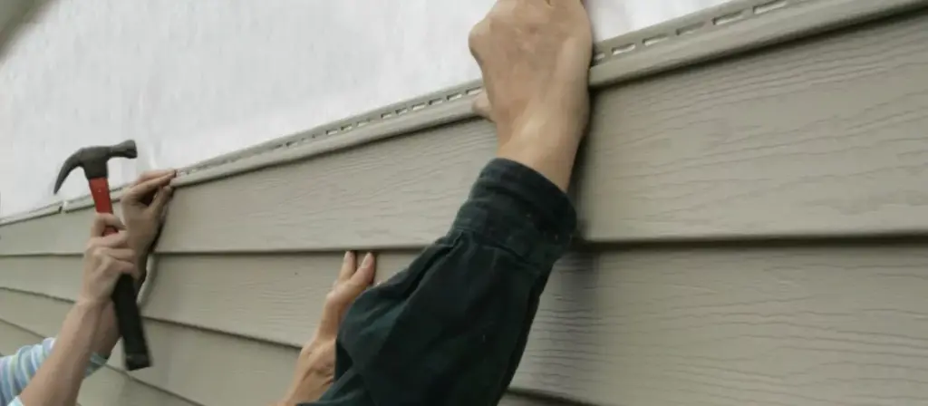Worker nailing a new siding panel in place with a hammer